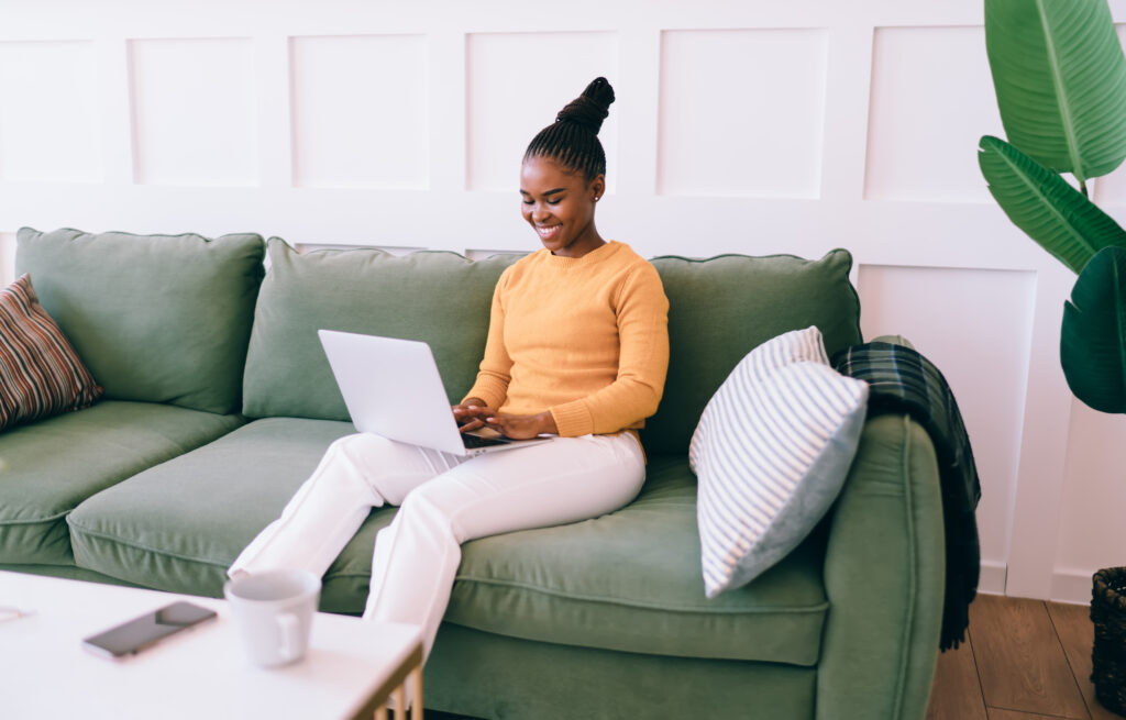 Black woman resting on sofa and using laptop